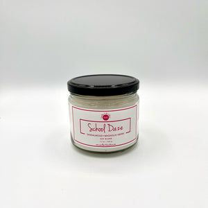 12 oz glass jar candle with cotton wicks and soy blend wax, crafted to enhance self-care and evoke nostalgia. White label with berry-colored text reads 'School Daze'. Fragrance is reminiscent of berry sorbet with hints of summer flowers, set on a background of soothing sandalwood and warm musk.