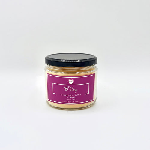 12 oz glass jar candle with cotton wicks and non-toxic fragrance. Soy blend wax scented with the aroma of cake with vanilla buttercream frosting. Magenta label reads 'B Day.' Perfect for celebrating with a sweet and indulgent scent.