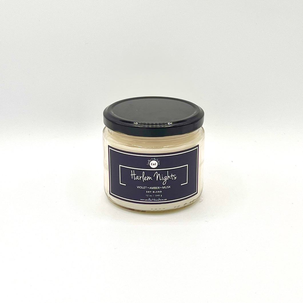 12 oz glass jar candle with cotton wicks and soy blend wax, featuring a non-toxic fragrance. Designed to evoke feelings of pride, self-worth, and nostalgia. Midnight blue label reads 'Harlem Nights'. Fragrance combines violet, amber, and musk for a powdery night-time scent.